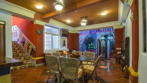 A dining area with a glass table and wicker chairs, a staircase with colorful tiles, and a view of a garden through a window. - Casa Virgilio B&B (Nuevo Nayarit)