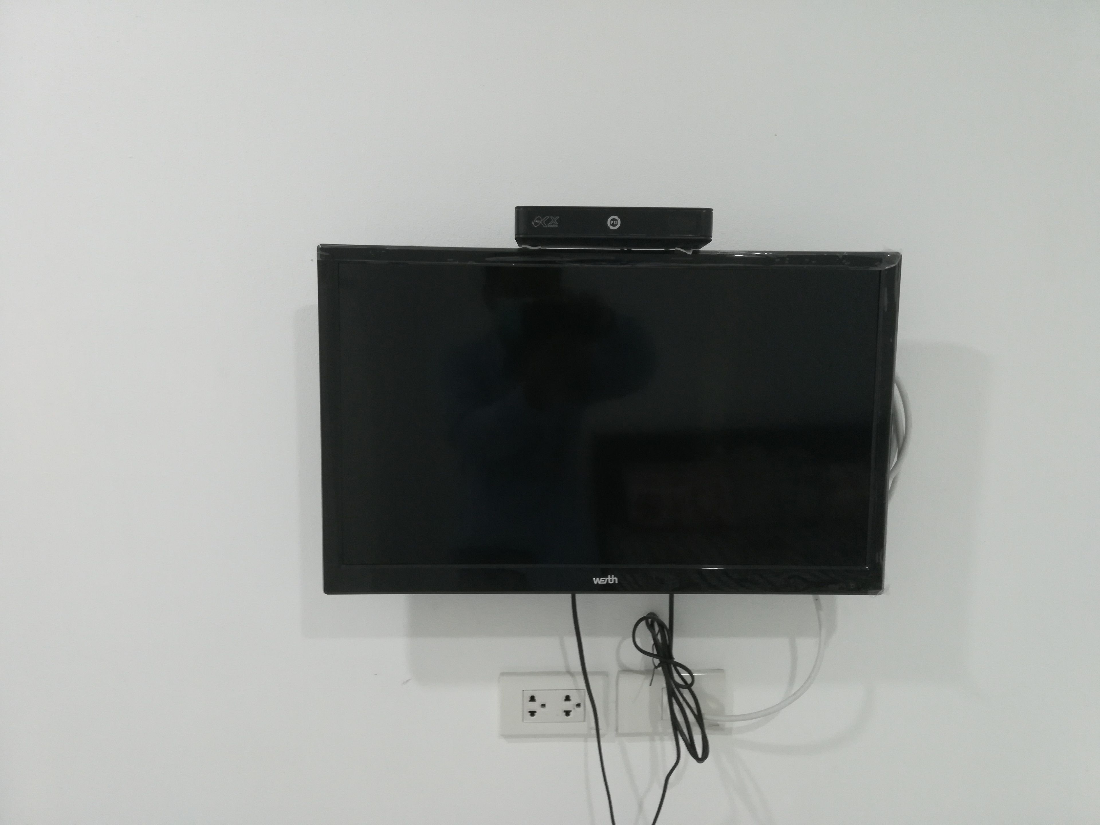 Televisor de pantalla plana montado en una pared blanca con un enchufe debajo.