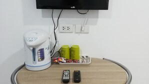 A small table with a kettle, two remote controls, and a tray with cups and snacks. - Sroe Ground Homestay (Sanom)