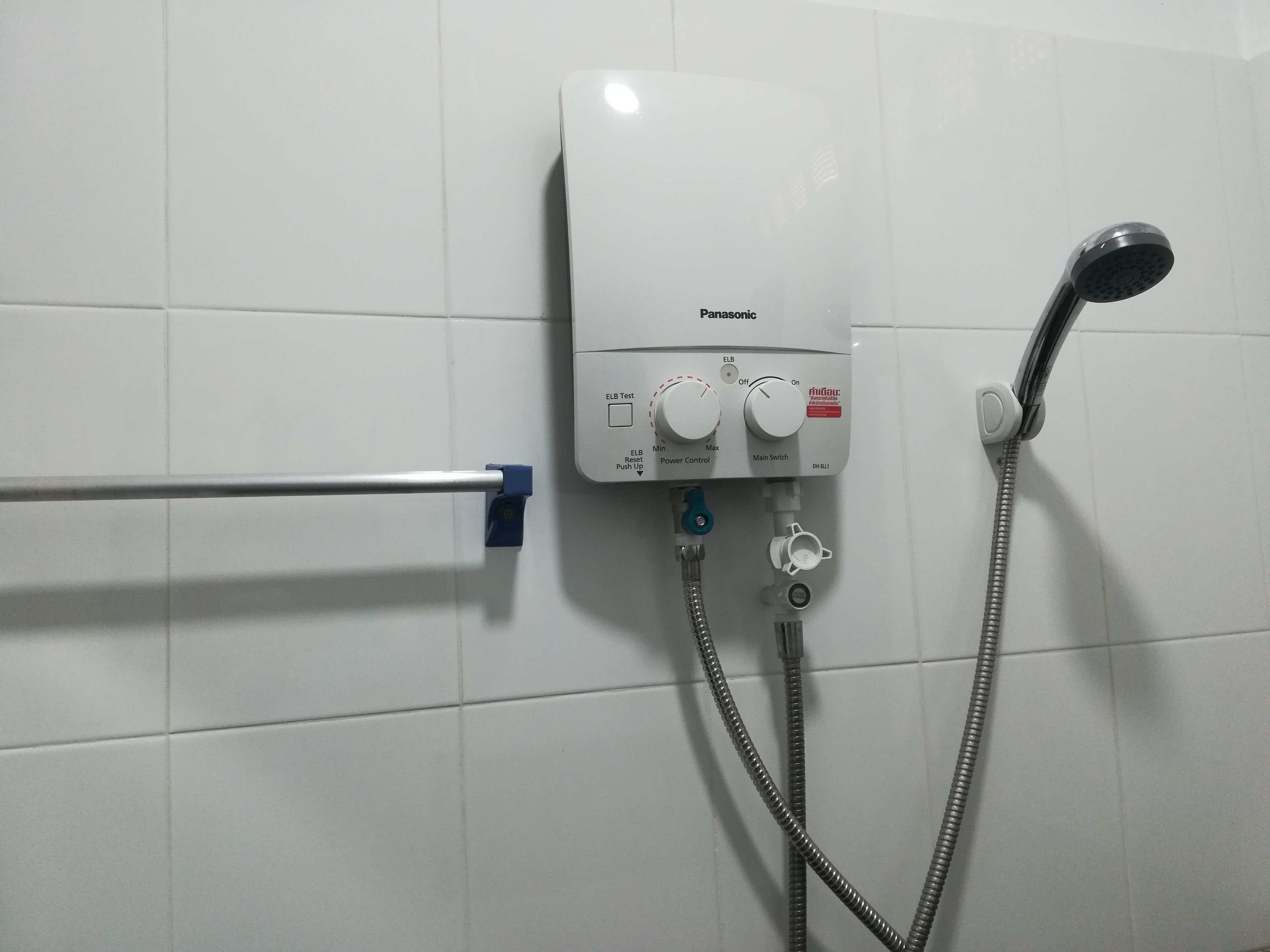 Un baño con pared de azulejos blancos, ducha de mano y panel de control con dos mandos y un botón.