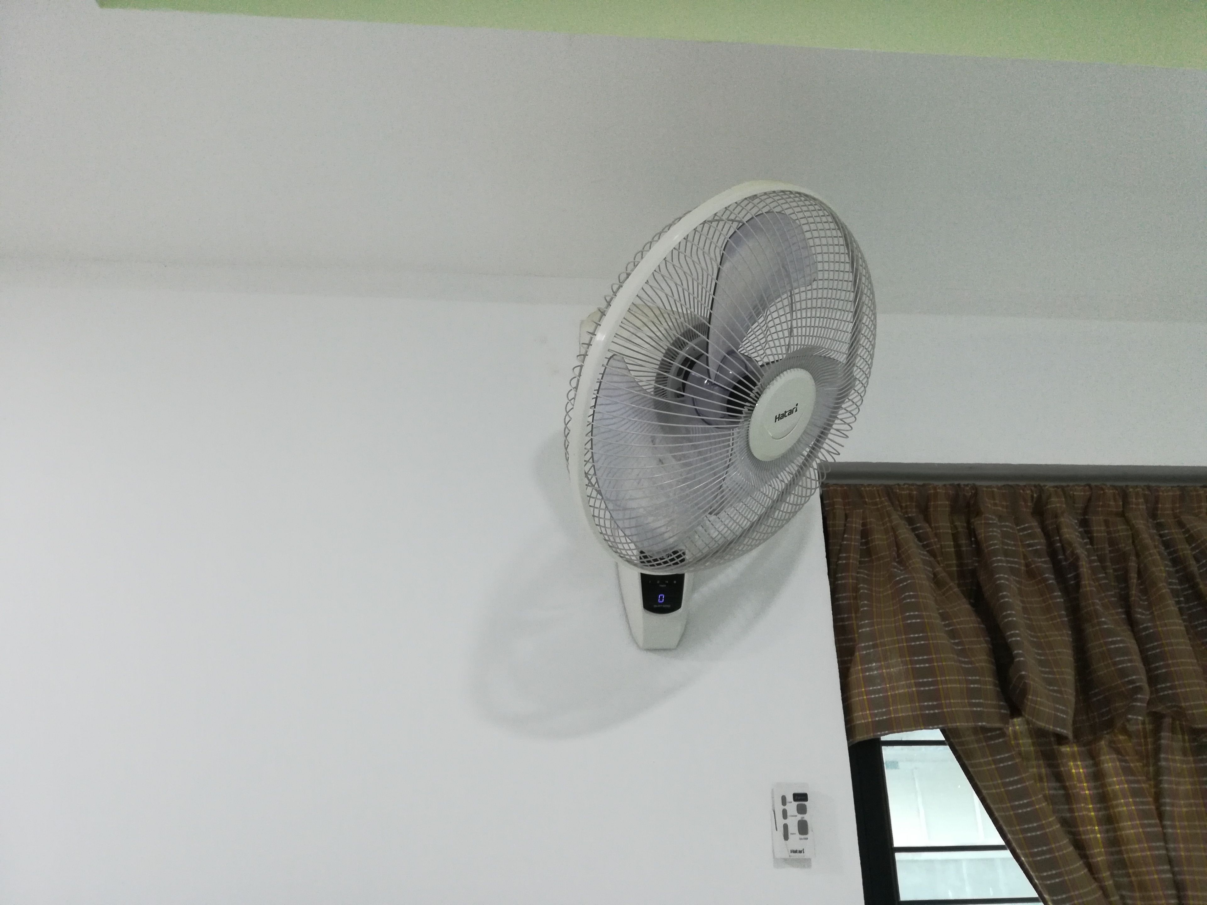 Ventilador de pie fijado a una pared blanca en una habitación con ventana y cortina.