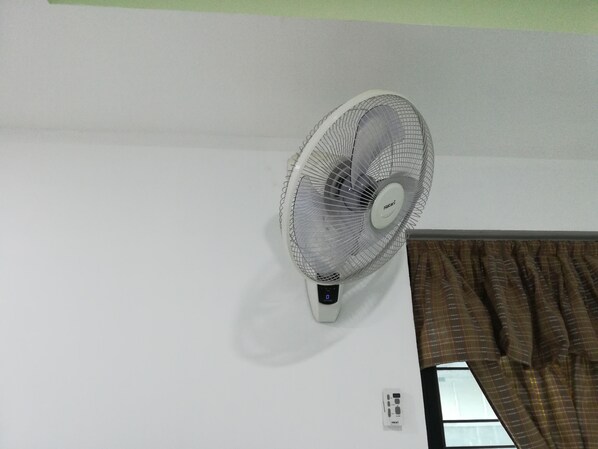 Ventilador de pie fijado a una pared blanca en una habitación con ventana y cortina.