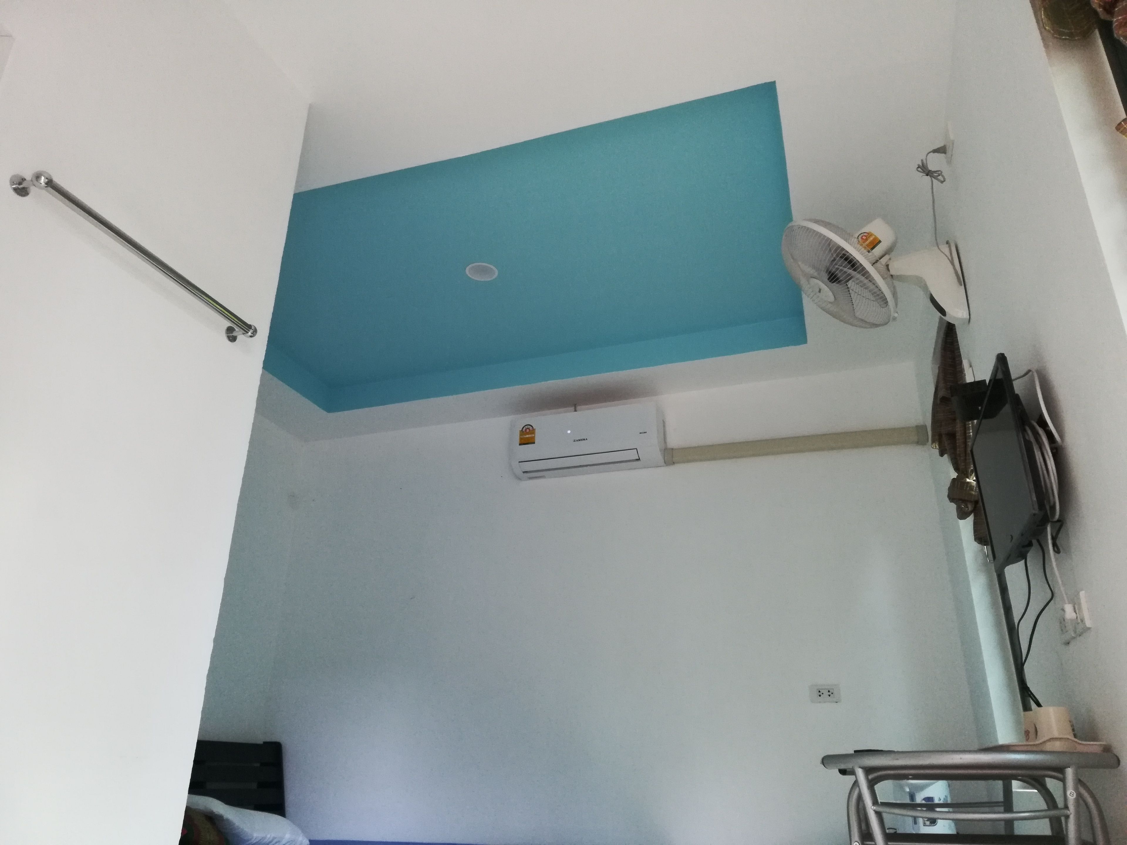 A room with a blue ceiling, an air conditioning unit, a ceiling fan, a television, and a bed.