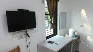 A small room with a desk, a television mounted on the wall, a window with blinds, a kettle, and a chair. - Sroe Ground Homestay (Sanom)