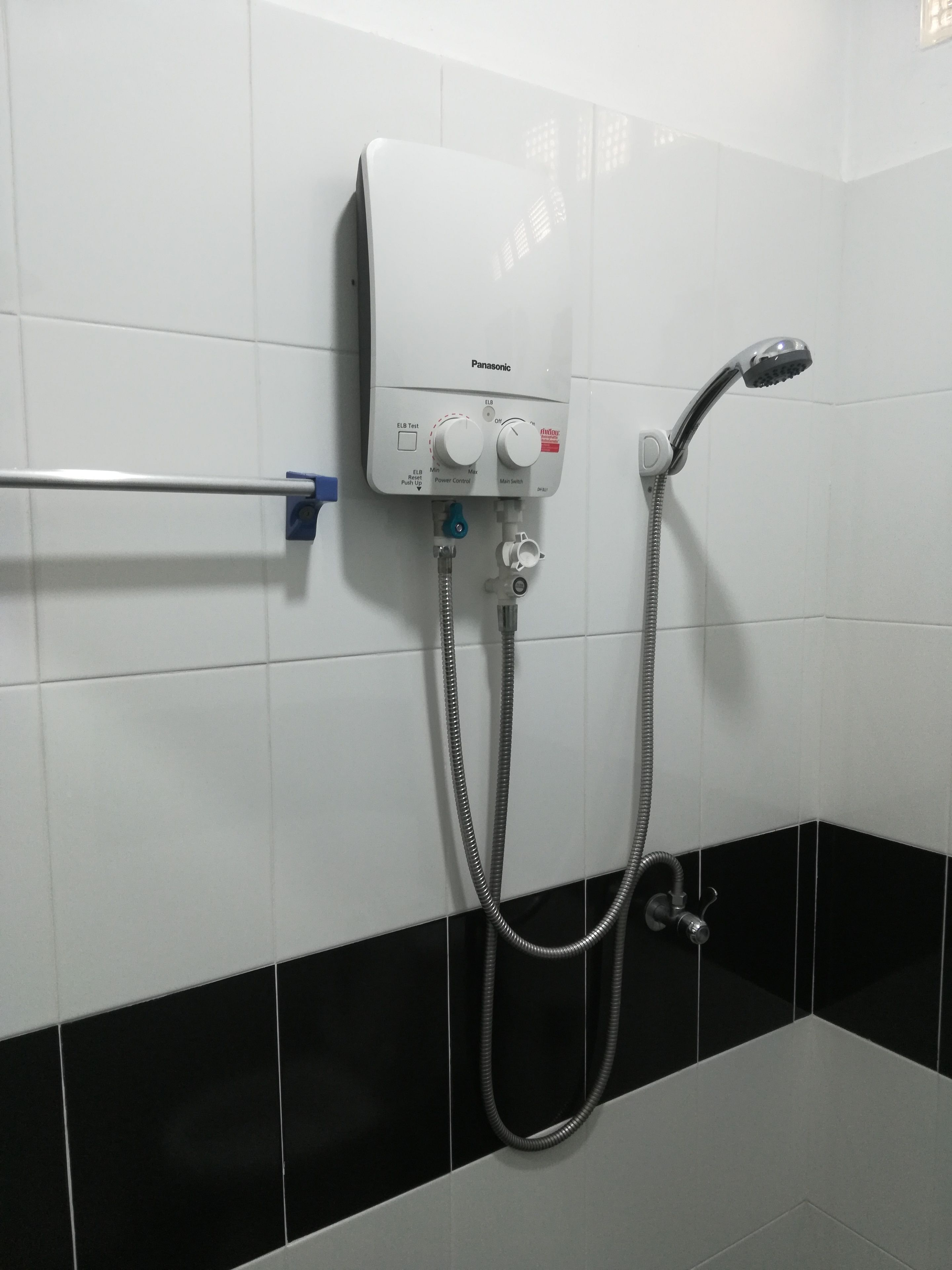 Un baño con pared de azulejos blancos y negros, una ducha eléctrica Panasonic y un perchero.