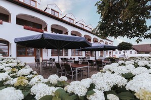 An outdoor seating area with tables and chairs, umbrellas, and white flowers. - Hotel Mörbischerhof (Morbisch am See)
