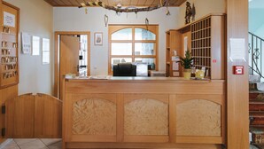 A reception desk with a wooden finish, a large arched window, and a staircase with wooden steps to the right. - Hotel Mörbischerhof (Morbisch am See)