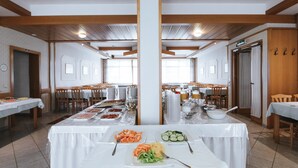 A buffet setup in a dining hall with multiple tables, chairs, and a variety of food items. - Hotel Mörbischerhof (Morbisch am See)