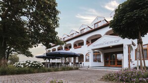 A white building with the name "MÖRISCHERHOF" on the facade, featuring outdoor seating with umbrellas, surrounded by greenery and flowers. - Hotel Mörbischerhof (Morbisch am See)