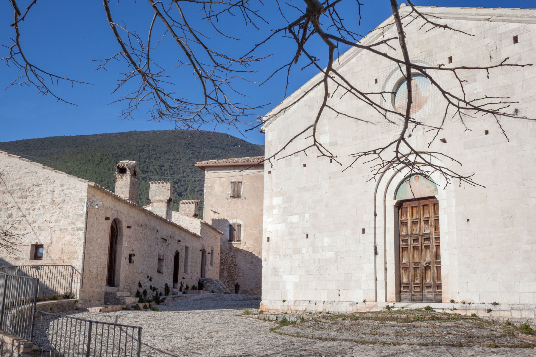 Un edificio histórico de piedra con una gran puerta de madera, un patio con pavimento de adoquines y una montaña al fondo.