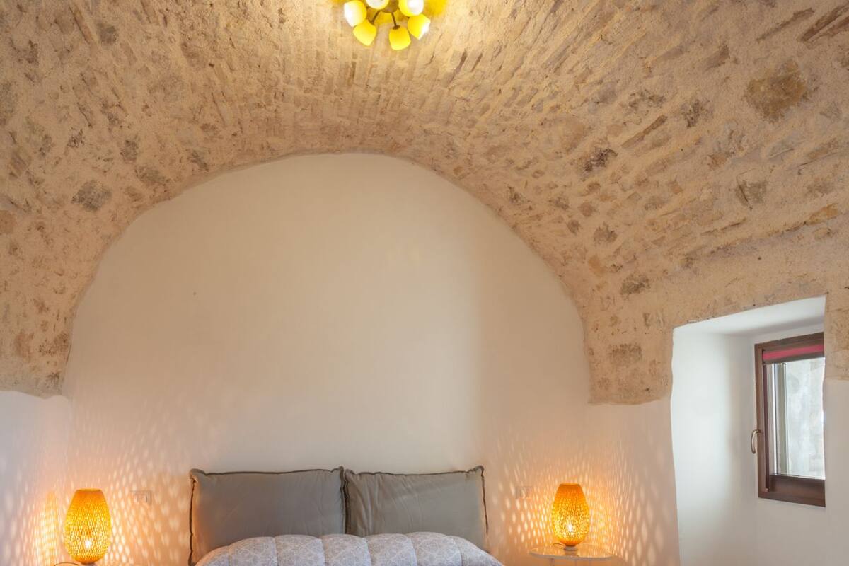 A bedroom with a large bed, two bedside lamps, and a unique arched ceiling.