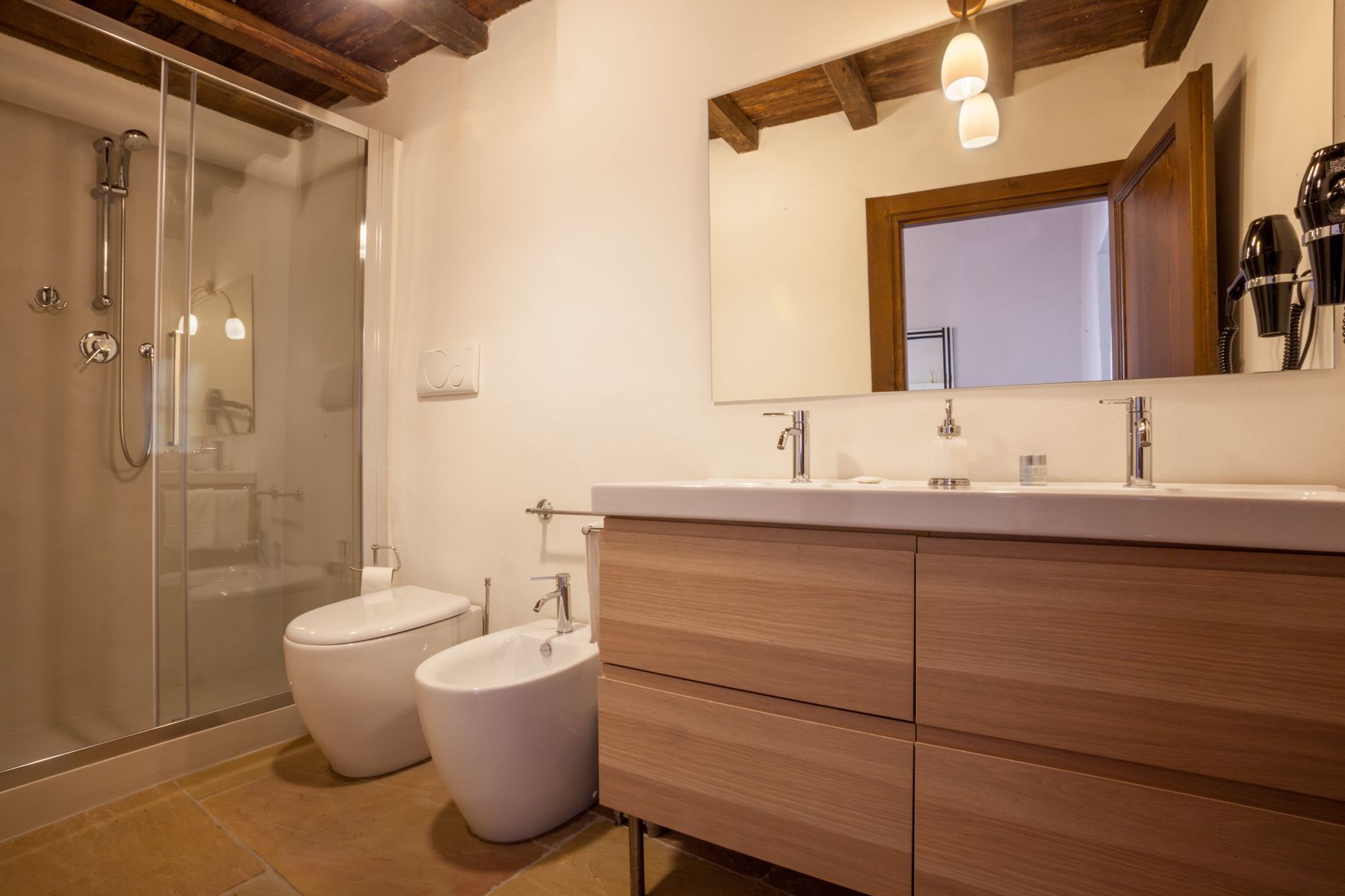 Un baño moderno con ducha de vidrio, dos inodoros, un tocador con espejo y armarios de madera.