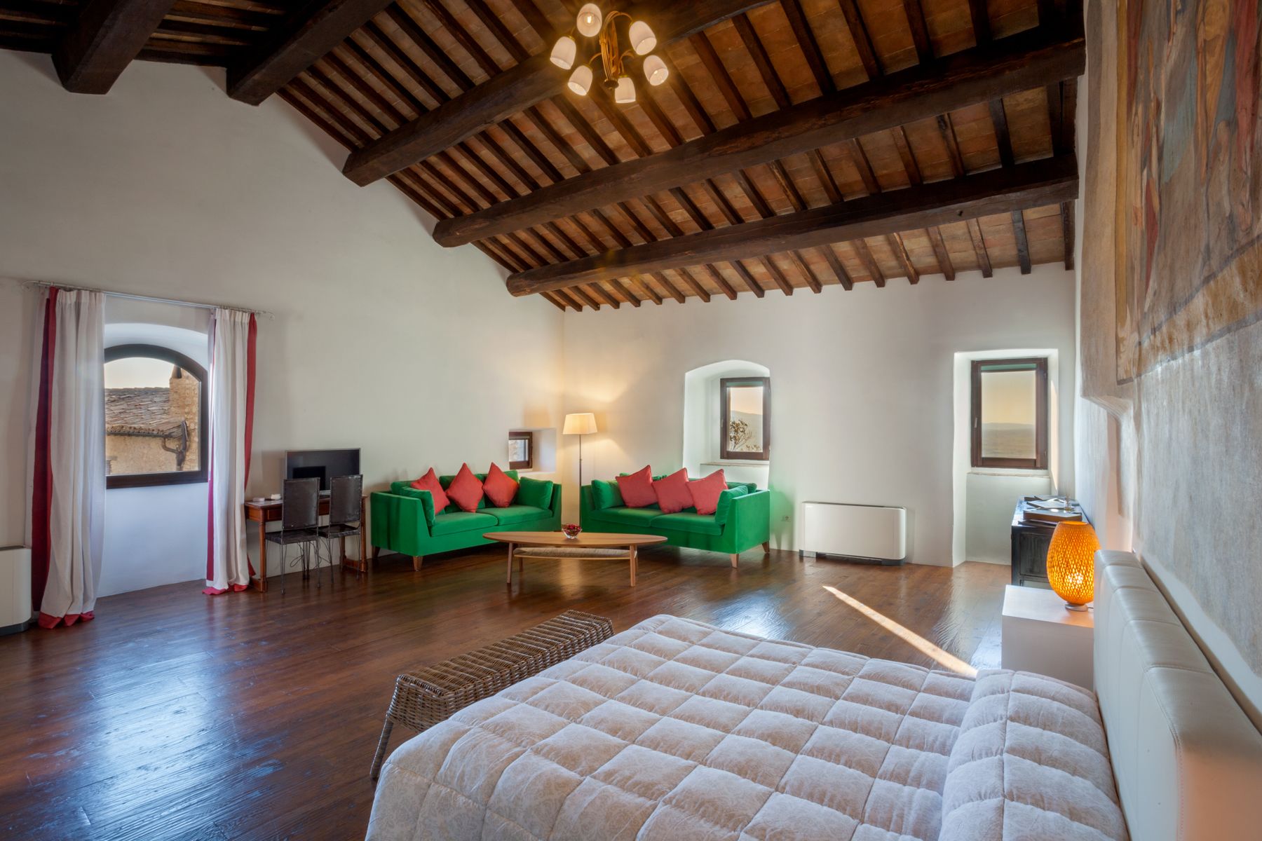 A spacious room with a high wooden ceiling, a green sofa with red cushions, a white bed, and a small table.