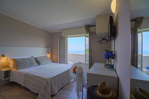 A hotel room with a bed, bedside table, lamp, and a view of the sea through a window. - Hotel Orizzonte Blu di Tropea (Ricadi)