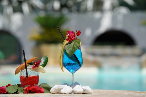 Two cocktails with garnishes and a pool in the background.