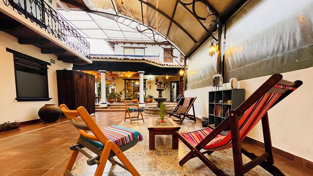 A spacious indoor area with a high ceiling, tiled floor, and a variety of seating options including wooden chairs and a rocking chair.