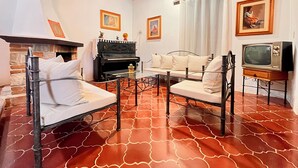 A living room with a fireplace, a piano, a sofa set, a television, and a chandelier.