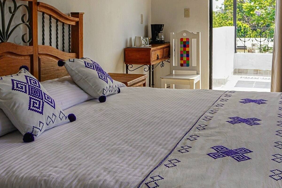 Un dormitorio con cama de madera, ropa de cama blanca y vistas a un área exterior a través de una puerta abierta.