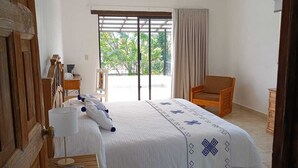 A bedroom with a bed, a chair, a desk, and a window with a view of greenery.