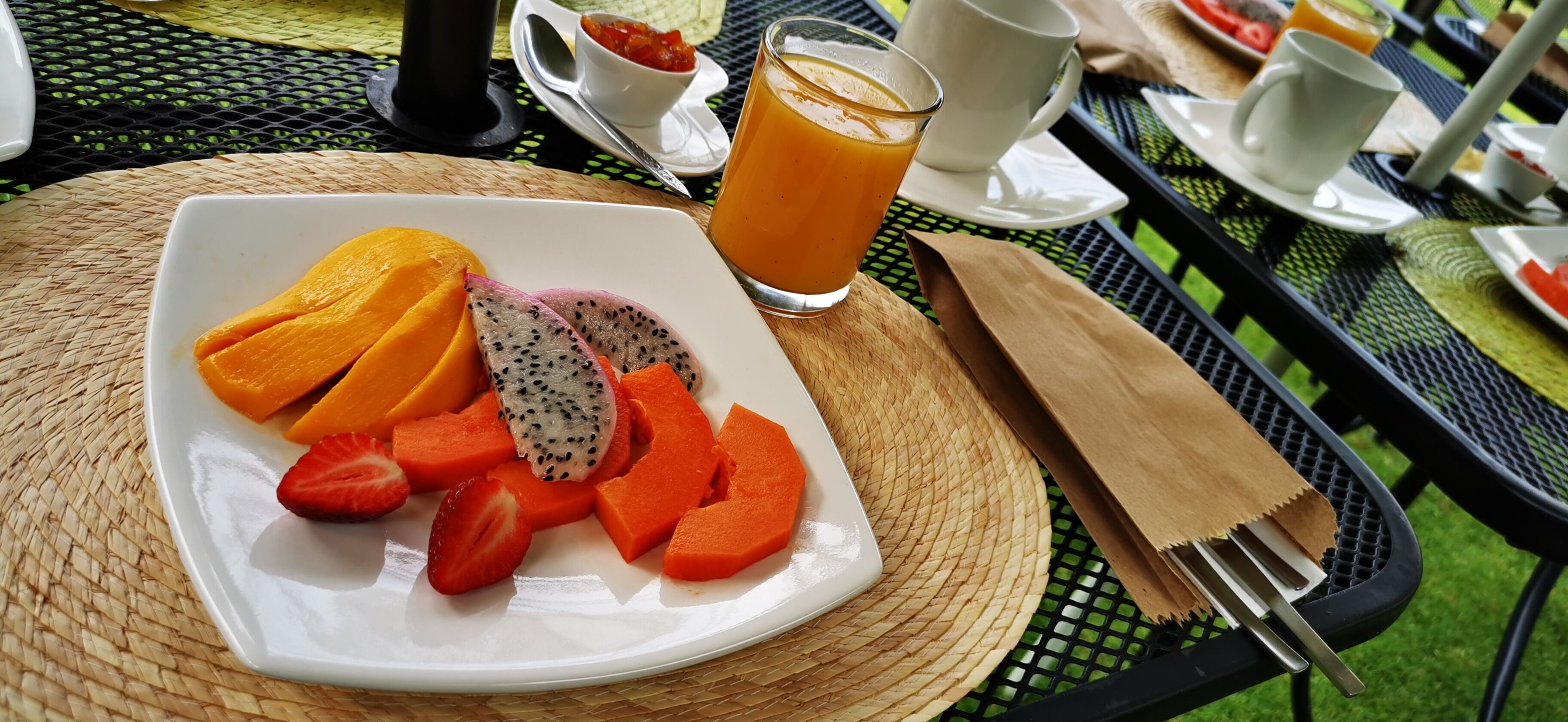 A breakfast setting with a plate of sliced fruits and a glass of orange juice on a table.