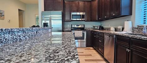 A modern kitchen with granite countertops, stainless steel appliances, and dark wooden cabinets.
