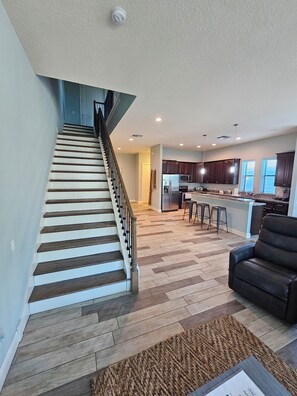 A spacious living area with a wooden staircase, a kitchen with dark cabinets, and a black leather sofa. - Luna: pool, 1 blk to the beach. 3b/3.5ba. beach items, longbrd, picklball close (Cocoa Beach)