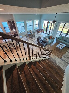 A spacious living area with a high ceiling, a wooden staircase, and a view of the outdoors through large windows.