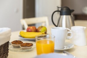 A breakfast table with muffins, a glass of orange juice, a coffee pot, and a plate with bananas and apples. - Quinta do Pé Descalço Guesthouse Sintra (Sintra)