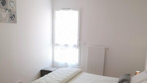 A bedroom with a bed, bedside tables, a window with curtains, a radiator, and a wall decoration.