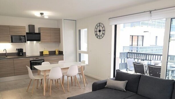 A modern apartment with a dining area, kitchen, and a balcony with outdoor seating.