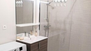 A modern bathroom with a built-in washing machine, a vanity with a mirror, and a glass-enclosed shower area.
