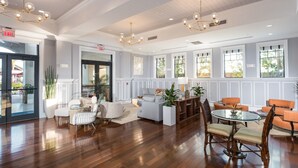 Un hall espacioso con suelo de madera, una zona de estar con sofás y sillones, y grandes ventanales que dejan entrar luz natural.