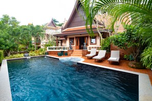 A swimming pool with lounge chairs, a hot tub, and a traditional building with a sloped roof.