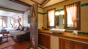 Una habitació d'hotel amb un llit, zona de seients, un mirall gran, un lavabo i armaris de fusta.