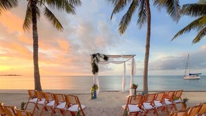 A beach wedding setup with a white arch and chairs arranged for guests.