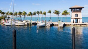 A marina with boats docked, a lighthouse, and palm trees.