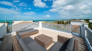 A rooftop terrace with wicker furniture, a view of the ocean, and a clear sky.
