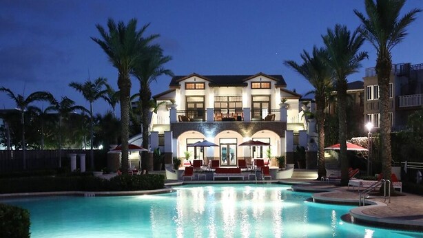 A large, multi-story hotel with a swimming pool, palm trees, and outdoor seating areas.