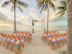 Decoración para una boda en la playa, con sillas y un arco adornado.
