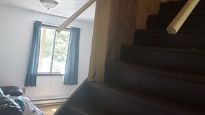 Una escalera con barandilla, una ventana con cortinas azules y una lámpara en el techo.
