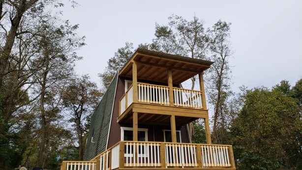 Una cabaña de madera de dos pisos con un balcón en el nivel superior, rodeada de árboles.