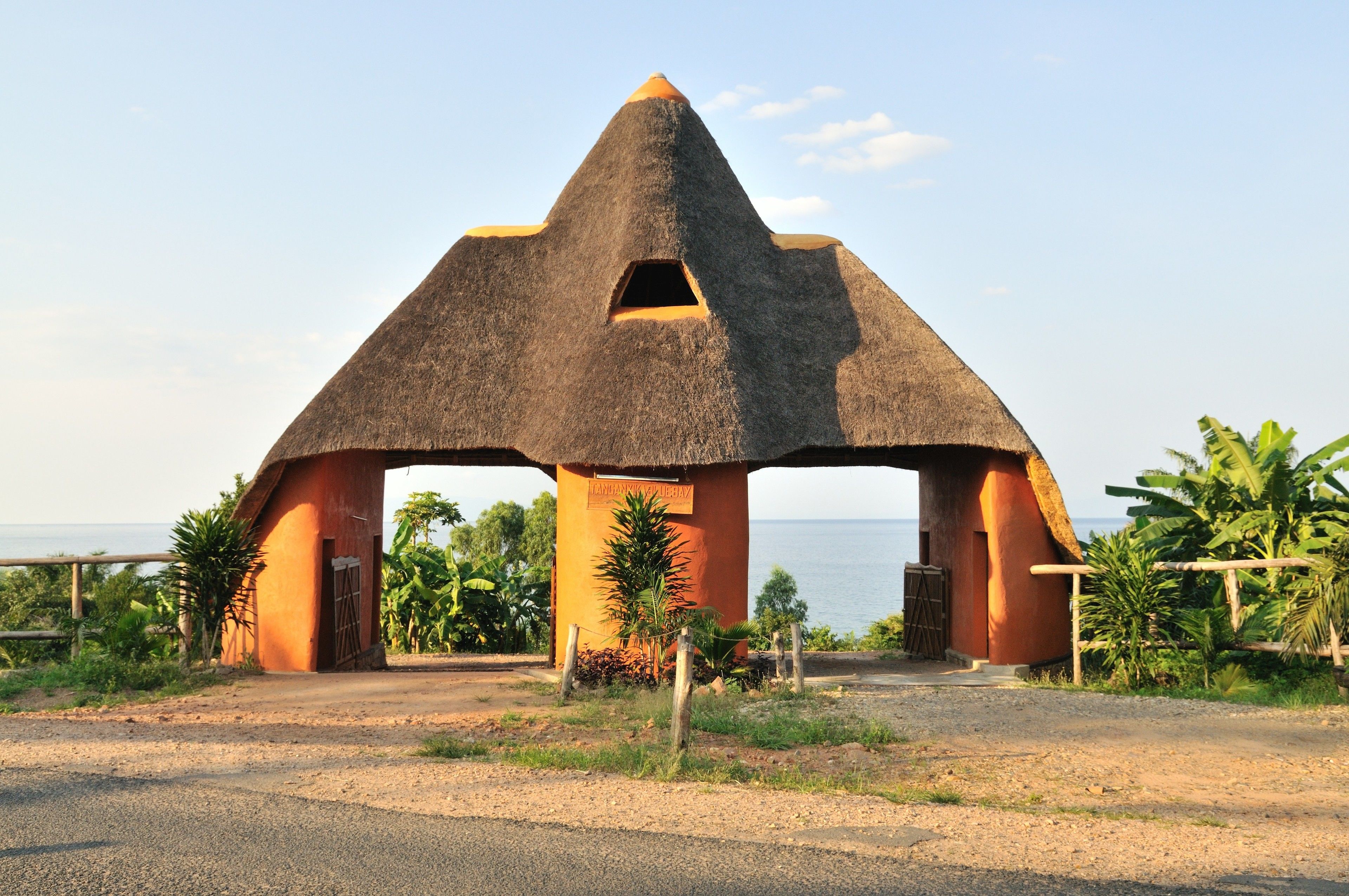 A unique thatched-roof structure with a central opening, surrounded by greenery and a clear view of the sea.