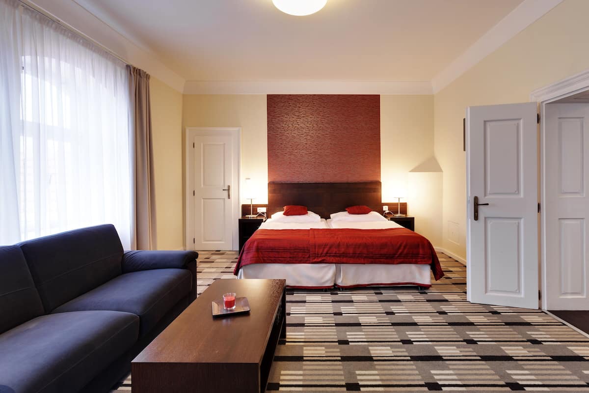A hotel room with a bed, a sofa, a coffee table, and a patterned carpet.