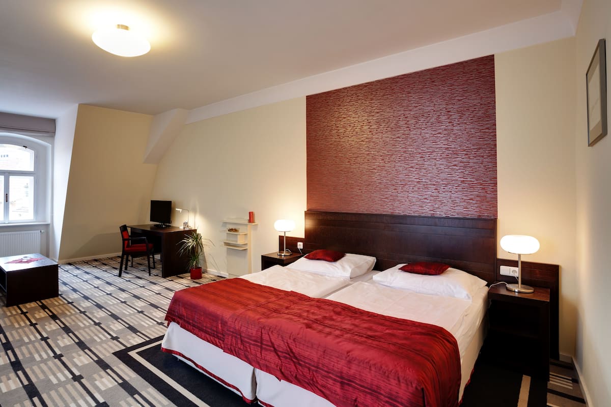 A hotel room with a bed, a desk, a chair, a TV, and a window.