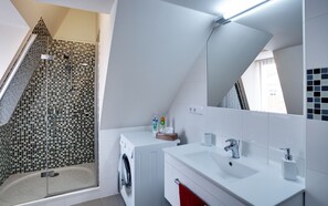 Un bagno moderno con doccia, lavatrice integrata, lavandino e uno specchio grande.