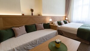 Une chambre d’hôtel avec un canapé, un lit, une table de chevet et une table sur laquelle est posé un vase de fleurs.