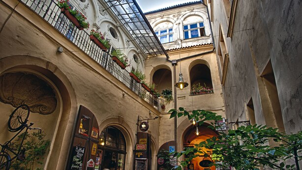 Une ruelle étroite bordée de portes en arc de cercle, un balcon orné de plantes en pot et des guirlandes lumineuses suspendues.