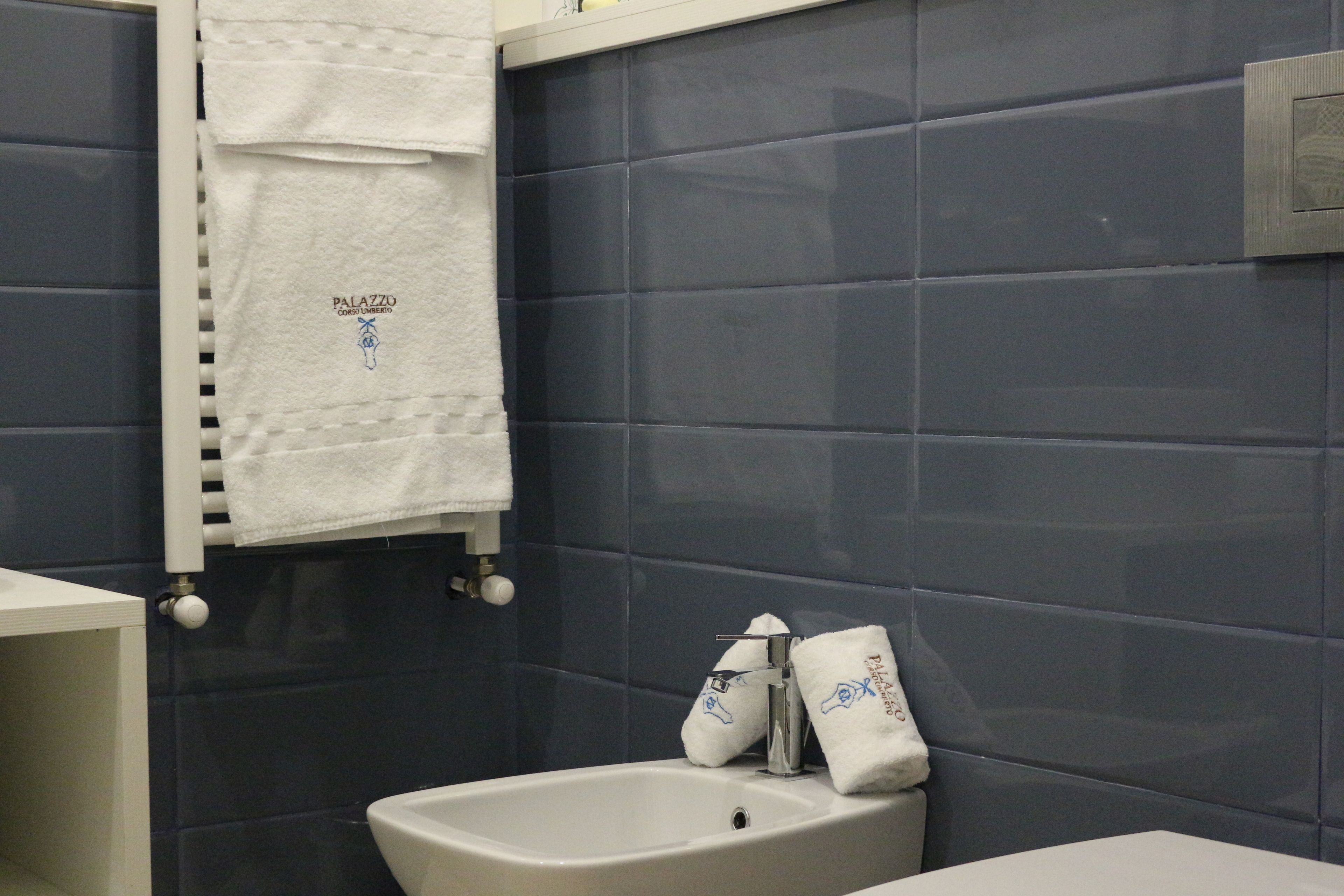A bathroom with dark blue tiles, a white sink, and two towels hanging on a towel rack.