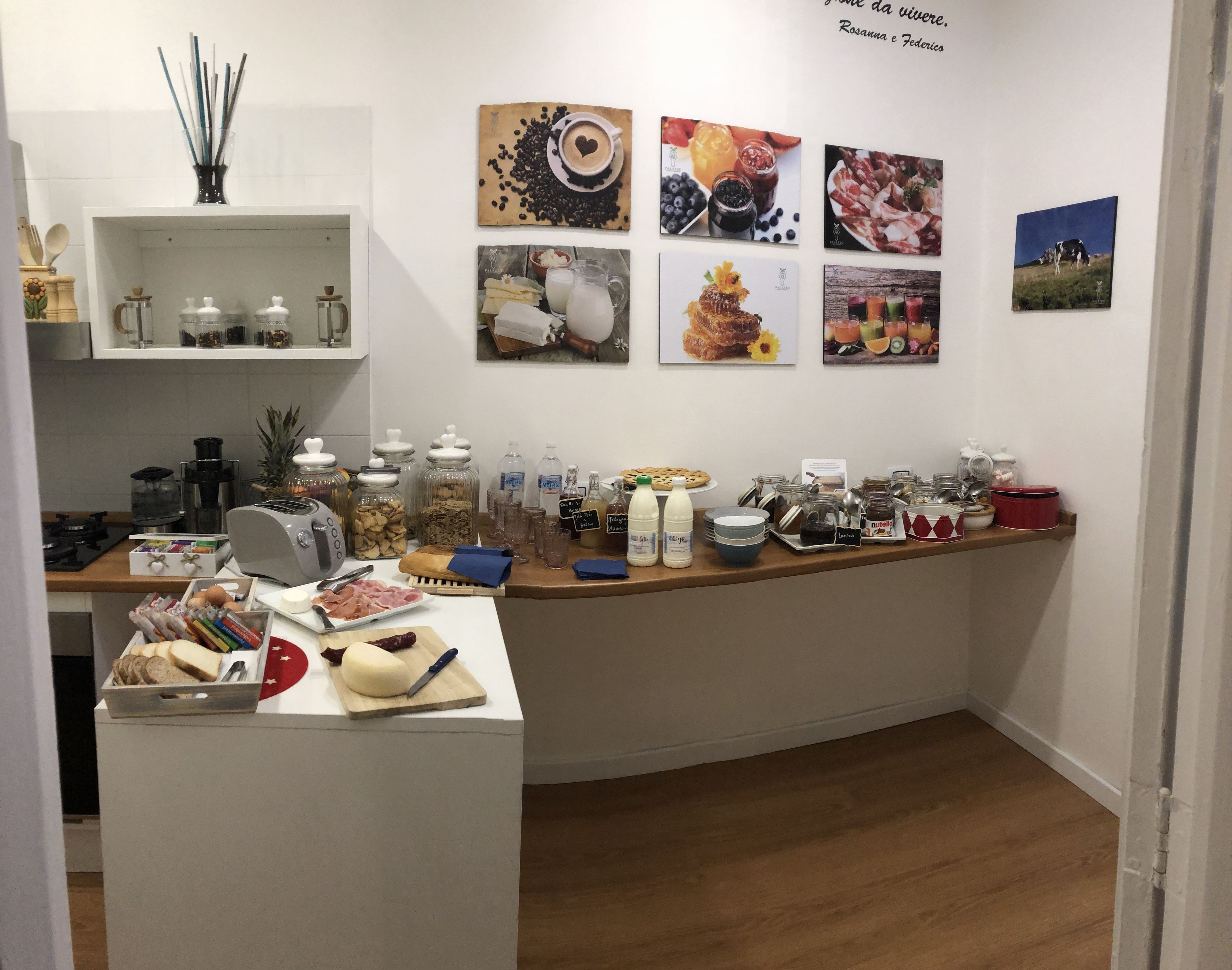 Una barra de desayuno con diversas opciones de comida y condimentos, una máquina de café y un refrigerador lleno de bebidas.