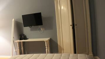Un dormitorio con cama, televisor montado en la pared, escritorio y armario.